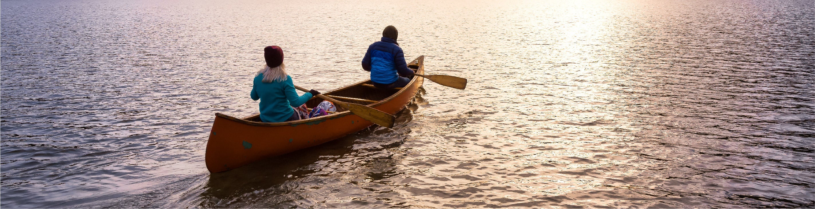 Two people in a canoe on a calm body of water at sunset.